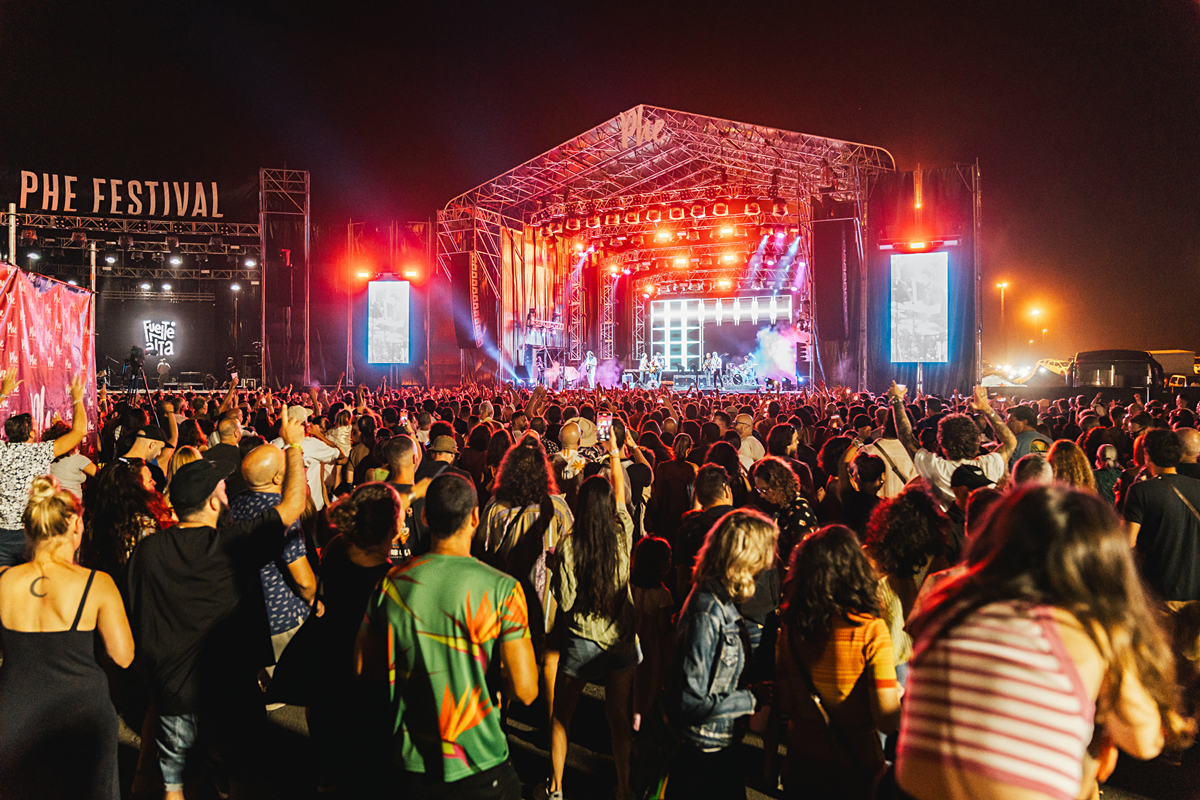 Personas disfrutando de música en directo en el festival PHE, con escenario iluminado y ambiente festivo.