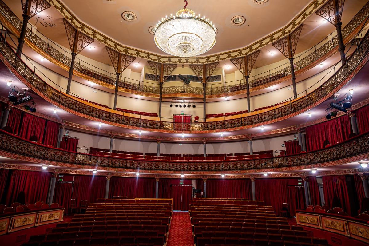 Interior del Gran Teatro de Cáceres con patio de butacas, escenario y ornamentación clásica iluminada en Cáceres.